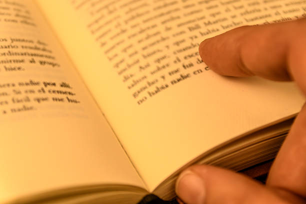 Close-up of a hand turning a book page with warm light and shallow depth of field. Concept of reading, learning and cozy evening.