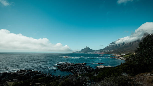 panoramic view from Lion's Head overlooking Camps Bay and the Twelve Apostles mountain range in Cape Town, South Africa. The turquoise Atlantic Ocean meets the white sands of Camps Bay beach, framed by dramatic peaks.