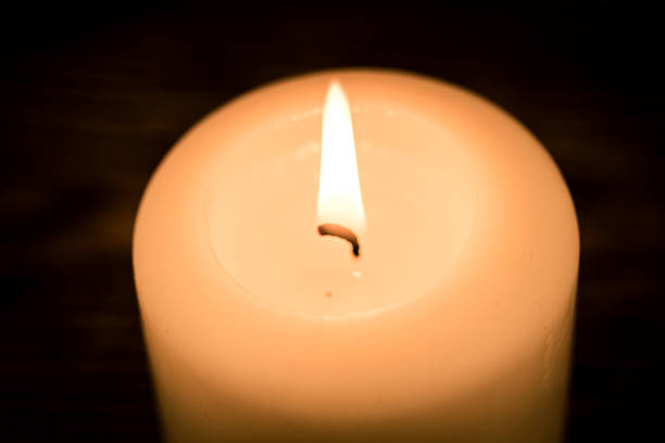 Macro close-up of a candle flame and wick with soft dark background. Warm minimal lighting concept for meditation, serenity and ambiance.