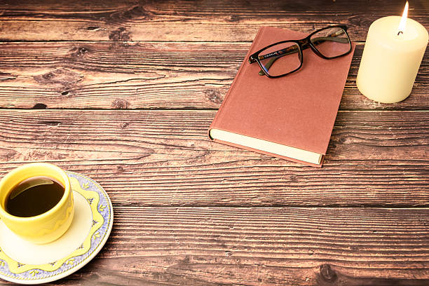 Wide rustic flat lay with coffee cup, closed book, eyeglasses and lit candle. Large copy space for ads, banners or blog headers.