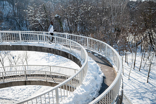 Man running on a winding concrete spiral bridge covered in snow, a winter park landscape in the background