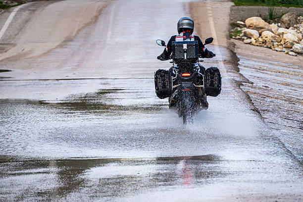 Back view of a motorcyclist splashing through a large water puddle on a wet road