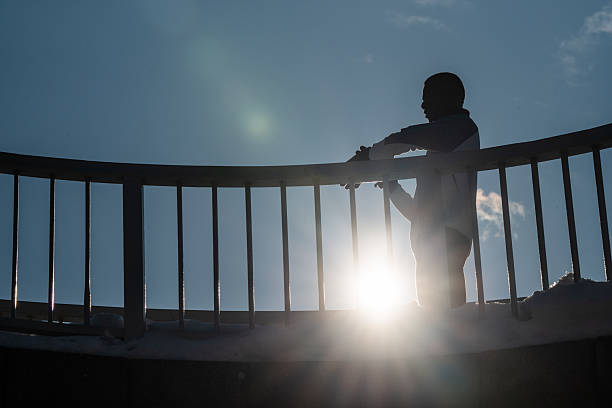 Man finding motivation, looking at the bright sun during a winter workout, resting on a bridge railing