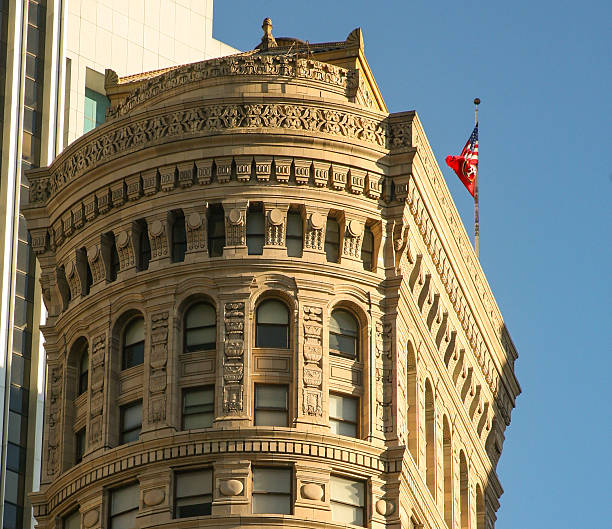 Ornate historic building with rounded corner tower, arched windows and detailed stonework, contrasted against a modern high‑rise in an urban skyline.
