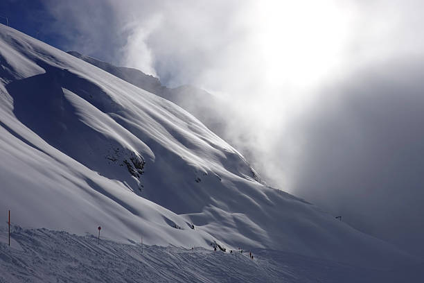 Ski piste cuts through the mountainside in the skiresort of St Anton am Arlberg on a cloudy hazy afternoon with misty snowcovered mountainrange in the background in the Arlberg Alps in Austria