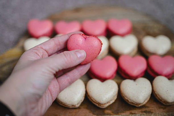 Hand holding a pink heart shaped macaron with more macarons in the background