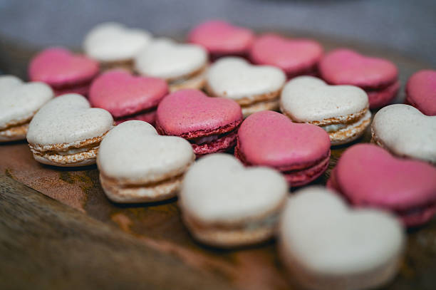 Heart shaped pink and white macarons arranged on a wooden surface