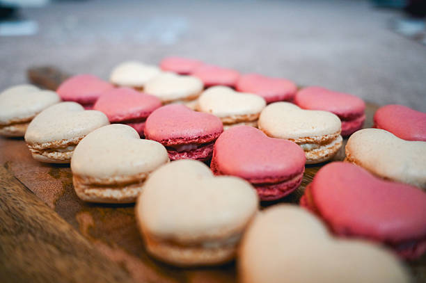 Pink and white heart shaped macarons resting on a wooden surface