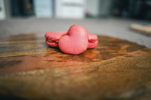 Heart shaped pink macarons resting on a rustic wooden surface