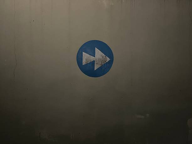 Blue circular sign with a white fast forward arrow painted on a textured, weathered concrete wall The grunge texture adds an urban industrial feel