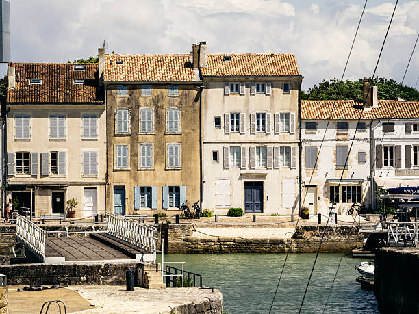 Pastel-toned historic buildings line the tranquil harbour of Saint-Martin-de-Re on Ile de Re, France, capturing timeless coastal village charm on a summer day.