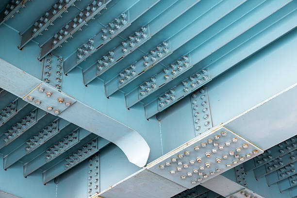A dramatic view of the underside of a teal-painted steel bridge, featuring riveted girders, repeating ribs, and structural spans. Ideal for architecture, engineering, infrastructure, and industry