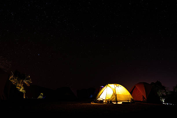 A camping tent with glowing light inside and beautiful night sky with starts as background. Photo contained some noise due to low light environment.