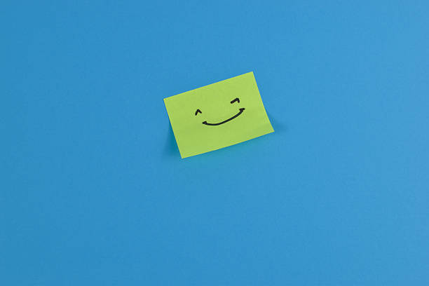 istock Green sticky note with cheerful smiley face on bright blue background, conveying positivity through bold color contrast and minimal design. 2257177388