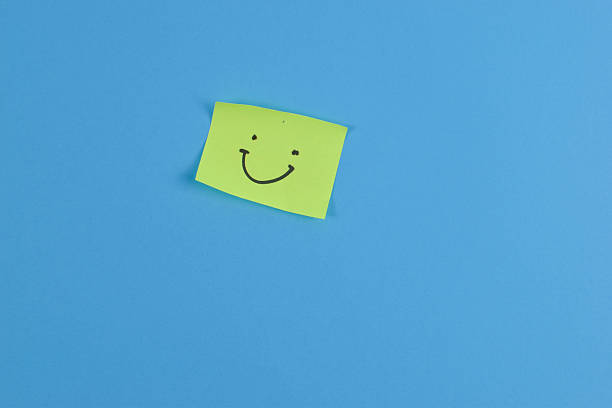 istock Green sticky note with cheerful smiley face on bright blue background, conveying positivity through bold color contrast and minimal design. 2257177389