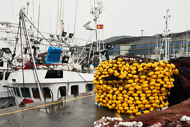 Fishing boats moored at a dock, with stacked fishing nets and numerous yellow floats ready for ocean work. Santoña, Cantabria