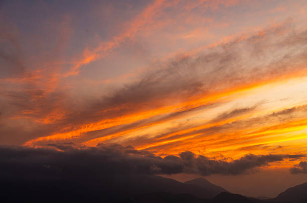 Beautiful bright orange sunset sky with clouds over the mountains silhouette.