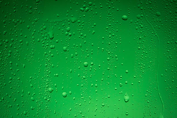 Close up of wet glass with dripping water drops and streaks of rain, on a bright green chroma key background, perfect for visual effects and background replacement.