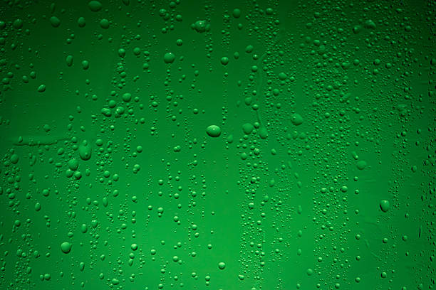 Close up of wet glass with dripping water drops and streaks of rain, on a bright green chroma key background, perfect for visual effects and background replacement.