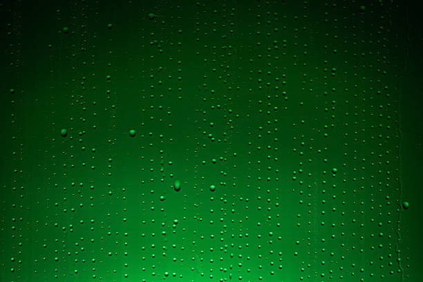 Close up of wet glass with dripping water drops and streaks of rain, on a bright green chroma key background, perfect for visual effects and background replacement.