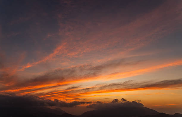 Beautiful bright orange sunset sky with clouds over the mountains silhouette.