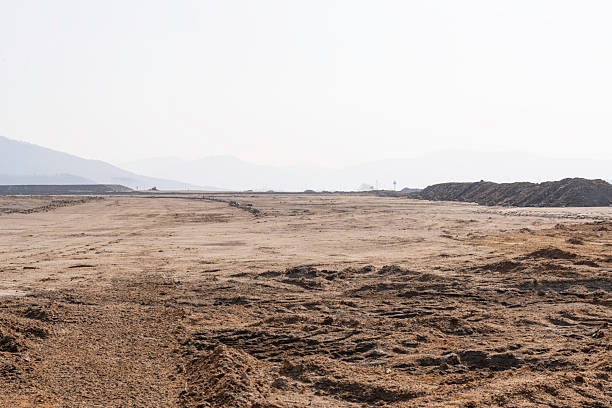 construction site with dirt road and barren land under clear sky, showing early stage infrastructure development and wide open space for future projects.