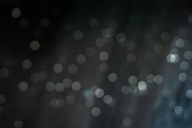 Blurred circular bokeh rays create a soft and dreamy abstract background in dark tones.