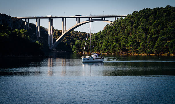 Sailing boat on open water  with forest and bridge  in the background