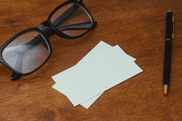 Two empty white business card templates for branding identity presentation. Eyeglasses and a pen on a dark wooden table, perfect for legal, corporate and financial consultant themes