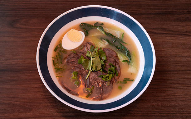 Ramen bowl with beef, egg, and fresh vegetables on table