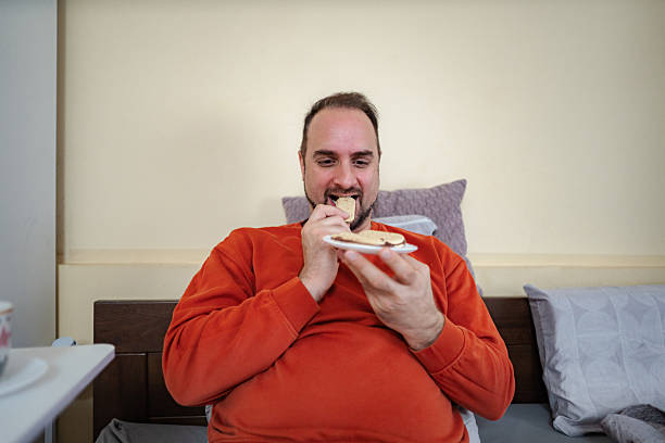 Man enjoying cookies while relaxing in bed, portraying unhealthy eating habits