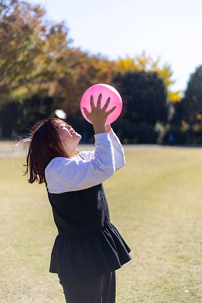 Mother playing with pink ball on grass field in public park