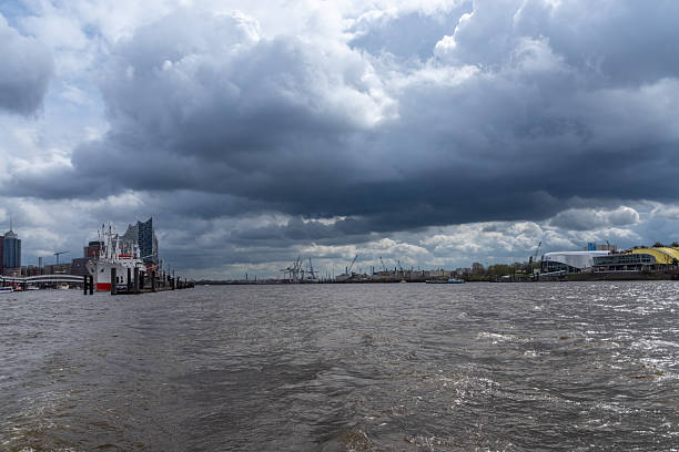 Elbe river flowing past Hamburg port and city waterfront under dramatic storm clouds. Hamburg, Germany