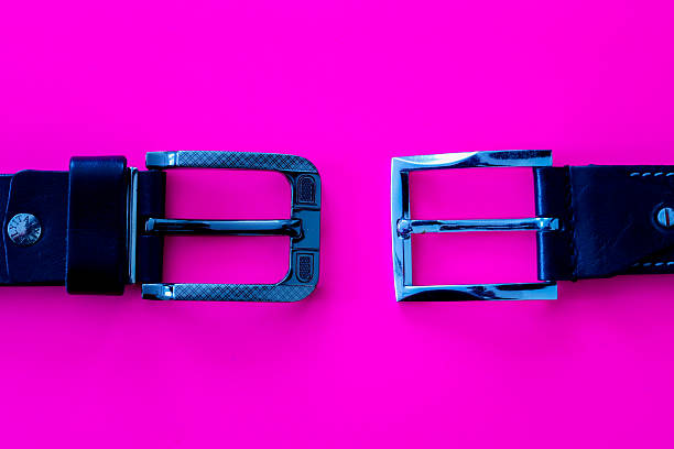 Two black leather belts with different metal buckles are located symmetrically opposite each other on a bright pink background.