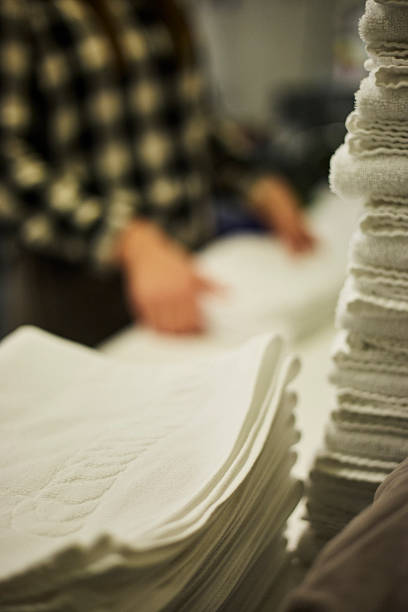 A hotel employee folding freshly laundered white towels in the laundry area. The scene conveys cleanliness, hospitality, and organized hotel operations. Suitable for concepts of travel, tourism, hotel service, housekeeping, and European accommodation.