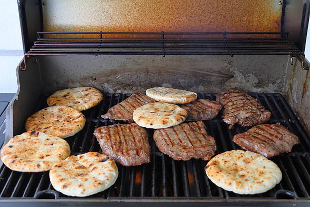 Indulge in the ultimate outdoor cooking experience with this mouthwatering image of a perfectly grilled steak, garnished with fresh herbs and accompanied by a plate of creamy rice. The stainless steel gas BBQ setup, complete with seasoning and utensils, sets the scene for a delightful culinary adventure. Ideal for marketing BBQ grills, cooking blogs, or food-related advertisements, this high-quality photo captures the essence of alfresco dining and summer gatherings.