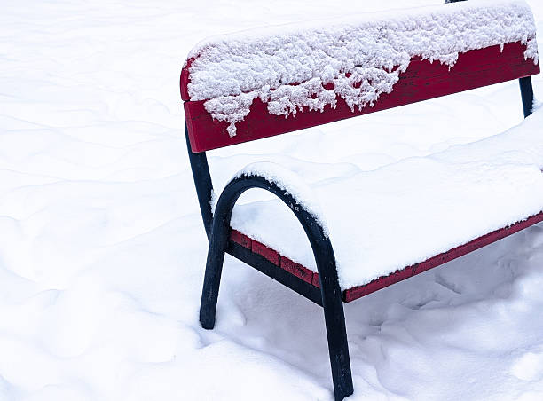 striking contrast shot of a bright red bench in a park during a heavy snowfall. The scene is calm and minimalist, with deep white snow surrounding the bench. Perfect for winter themes, urban solitude, and seasonal weather concepts