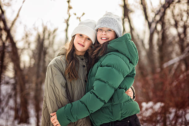 This is a summer image outdoors in bright sunlight. Twin sisters are hugging each other smiling at the camera. They're happy, relaxed, and enjoying their vacation.