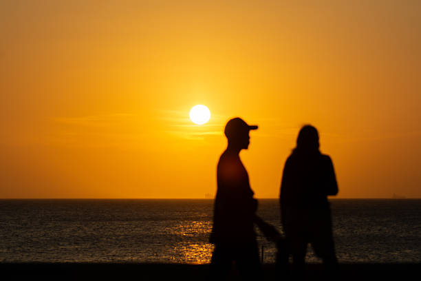 Salvador, Bahia, Brazil - January 2, 2026: Dramatic orange sunset on the horizon with silhouettes of people passing by. City of Salvador, Bahia.