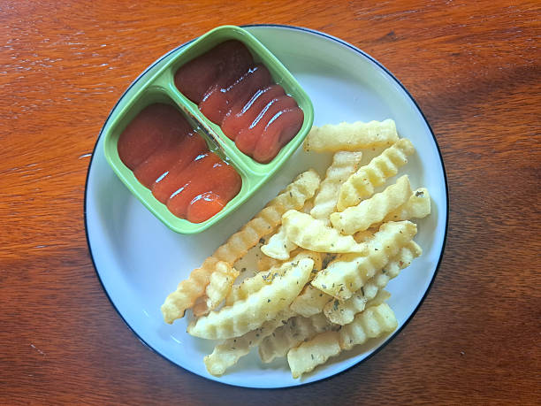 A turquoise plate with pommes frites, with mayonnaise and ketchup, accompanied by sausages. In the background a ketchup bottle and a mayonnaise bottle out of focus.