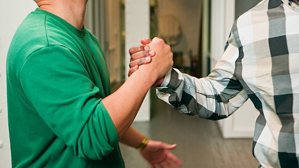 Two individuals clasp a firm handshake inside a bright hallway, conveying cooperation and mutual respect. The image highlights teamwork, partnership, and positive communication between colleagues or friends in a casual setting.