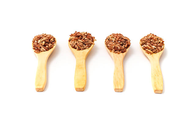 Four wooden spoons holding brown rice, presented against a clean white backdrop.