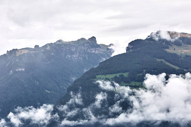 Breathtaking summer landscape of the Swiss Alps featuring majestic mountain peaks, lush green slopes, and dramatic clouds drifting across a blue sky. This natural scenery captures the beauty, freshness, and tranquility of Switzerland in summer, ideal for travel, nature, tourism, and outdoor adventure concepts.