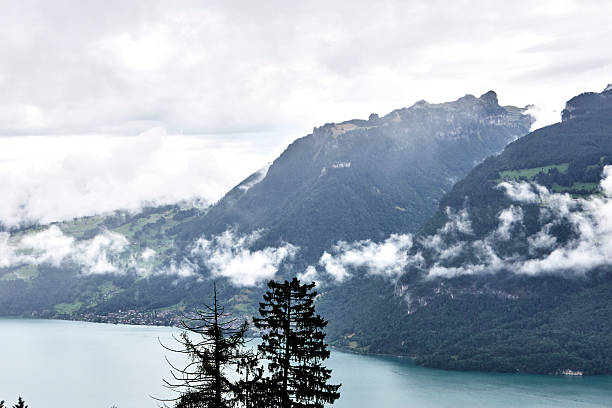 Breathtaking summer landscape of the Swiss Alps featuring majestic mountain peaks, lush green slopes, and dramatic clouds drifting across a blue sky. This natural scenery captures the beauty, freshness, and tranquility of Switzerland in summer, ideal for travel, nature, tourism, and outdoor adventure concepts.
