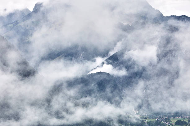 Breathtaking summer landscape of the Swiss Alps featuring majestic mountain peaks, lush green slopes, and dramatic clouds drifting across a blue sky. This natural scenery captures the beauty, freshness, and tranquility of Switzerland in summer, ideal for travel, nature, tourism, and outdoor adventure concepts.