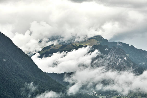 Breathtaking summer landscape of the Swiss Alps featuring majestic mountain peaks, lush green slopes, and dramatic clouds drifting across a blue sky. This natural scenery captures the beauty, freshness, and tranquility of Switzerland in summer, ideal for travel, nature, tourism, and outdoor adventure concepts.