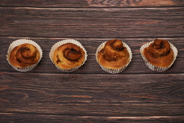 A row of four delicious cinnamon swirl pastries served in paper cups on a dark, textured wooden background.