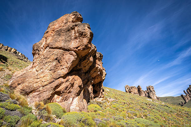 Close perspective of a tall rock formation emerging from green hills under a deep blue sky. The image highlights the unique shapes created by wind and time in southern Chile.