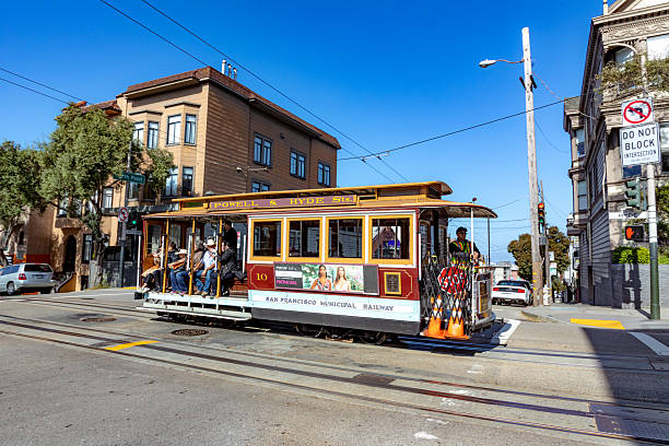 People ride cable car in San Francisco, California, USA on a sunny day.