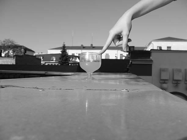 Minimalist black and white photo of a human hand gently touching a glass on a flat surface. Concept of decision, control, balance, fragility, hesitation and human interaction with objects. Abstract composition with copy space.